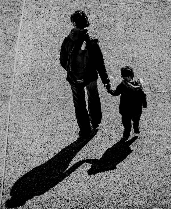 Mother and child on an open road, photographed from behind.
